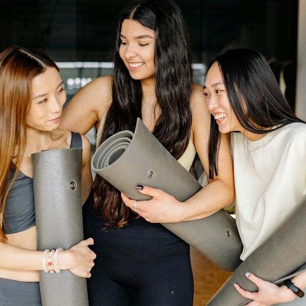 Two women smiling and supporting each other during a yoga class.